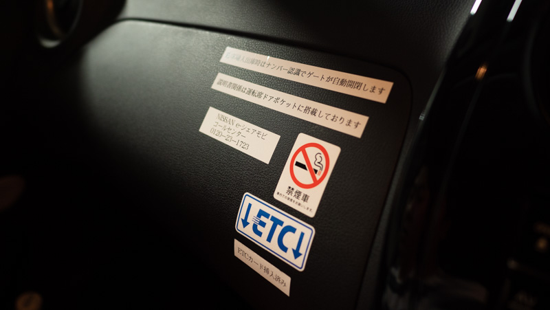 日産 e-シェアモビの日産ノートのグローブボックスに貼られているテプラなどのシール。禁煙、ETC備え付け、出入庫時は自動で行われる旨が案内されている。